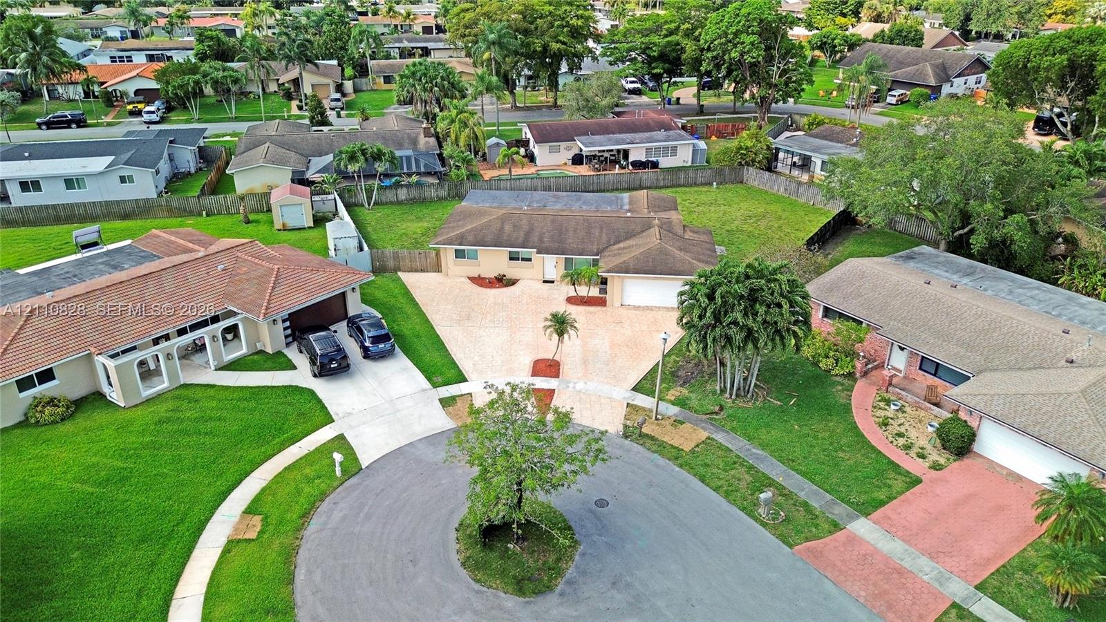 Aerial perspective of a single-story residence situated on a cul-de-sac lot, featuring a paver driveway, an attached garage, and a fenced backyard