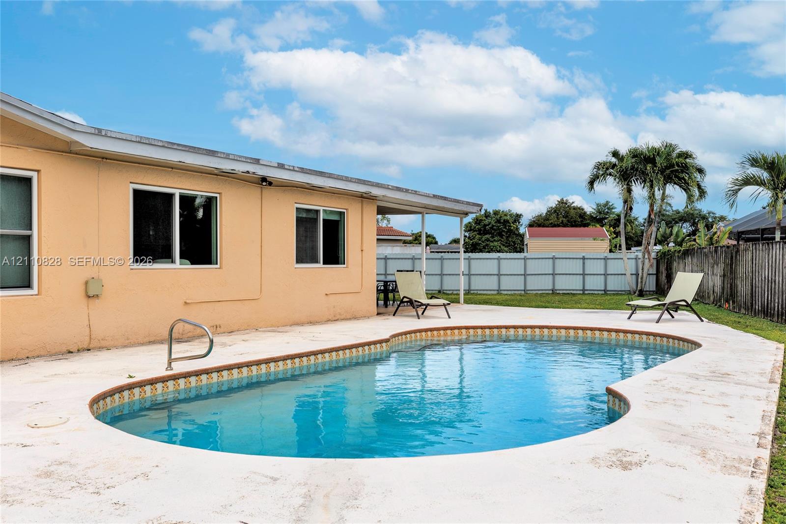 In-ground swimming pool with a concrete pool deck, covered patio, and perimeter fencing