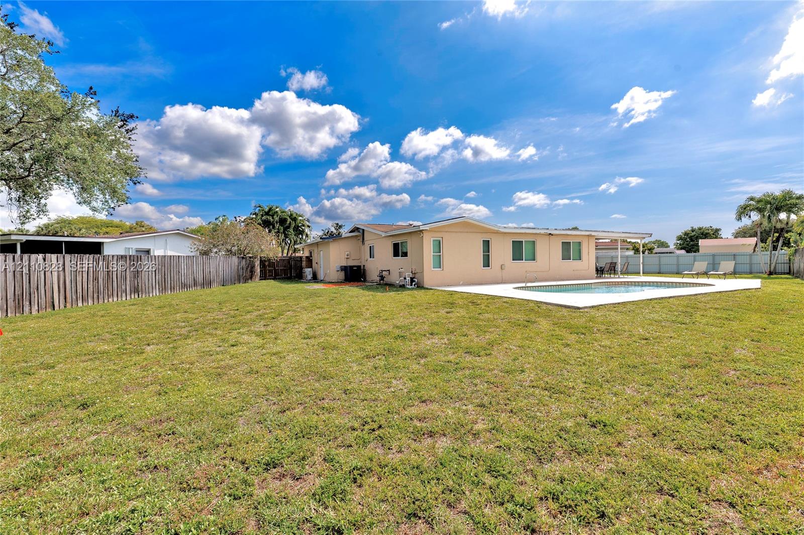 Expansive backyard featuring a concrete pool deck, in-ground swimming pool, wood privacy fencing, and a covered rear patio