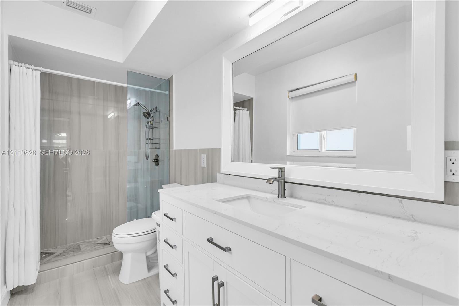 White shaker-style vanity with a quartz countertop, integrated rectangular sink, brushed-metal faucet, and large-format tile shower surround with a glass enclosure