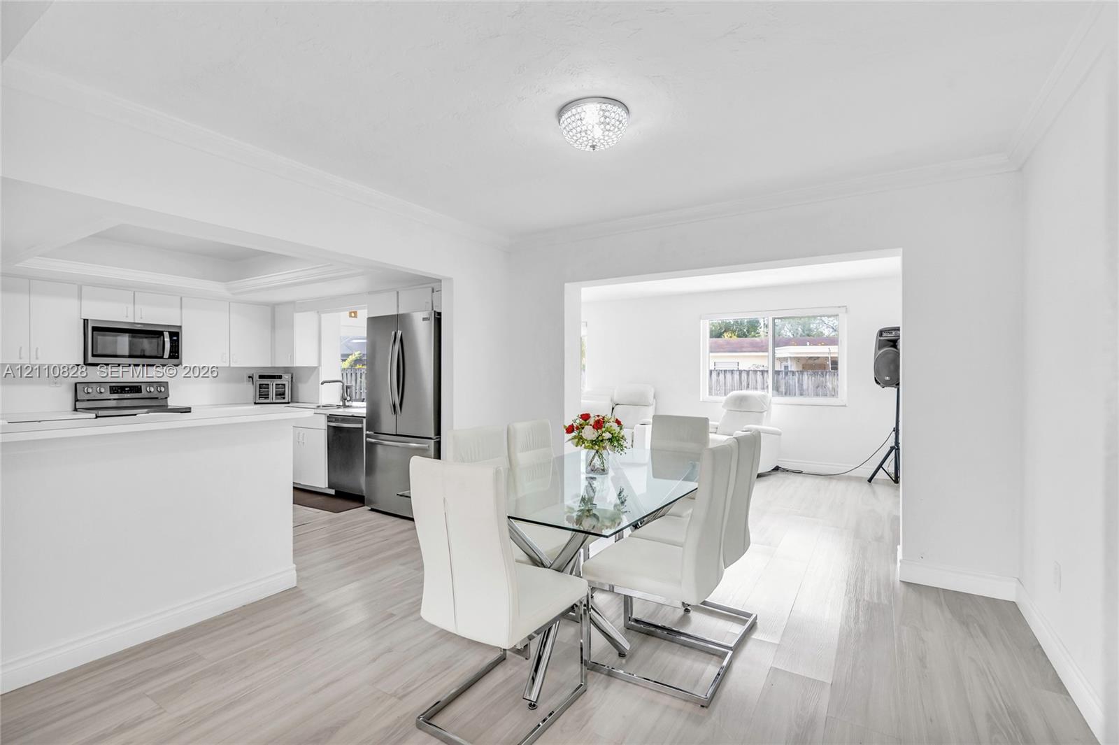 Open-concept space featuring wood-finish flooring, white cabinetry, stainless steel appliances, recessed tray ceiling, and a crystal-style flush-mount light fixture