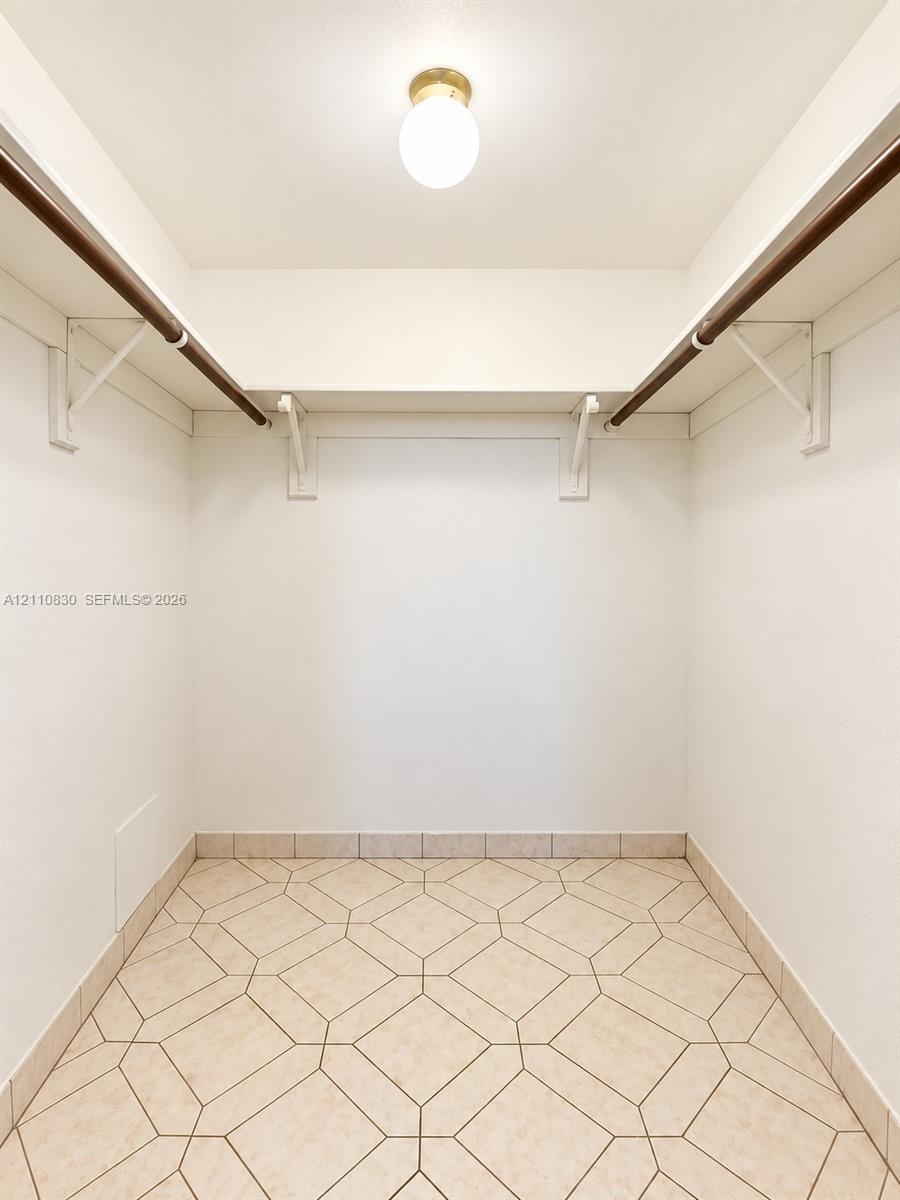 Storage space featuring geometric-patterned tile flooring, dual upper shelving with integrated hanging rods, and a circular flush-mount globe light fixture