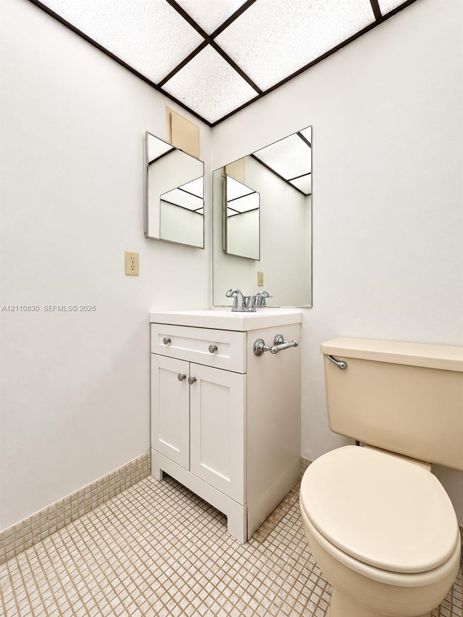 White shaker-style vanity with a square sink, chrome-finish dual-handle faucet, grid-pattern ceiling light, and mosaic-tiled flooring White shaker-style vanity with a square sink, chrome-finish dual-handle faucet, grid-pattern ceiling light, and mosaic-tiled flooring