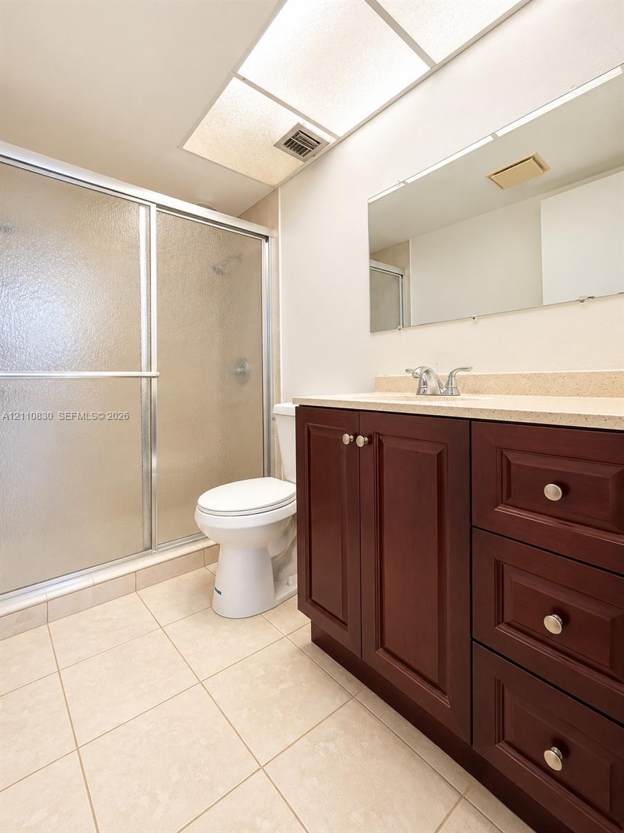 Spa-inspired primary bathroom featuring a custom wood-finish vanity with multiple drawers and brushed nickel hardware, ceramic tile flooring, and a frameless glass-enclosed shower with tile surround