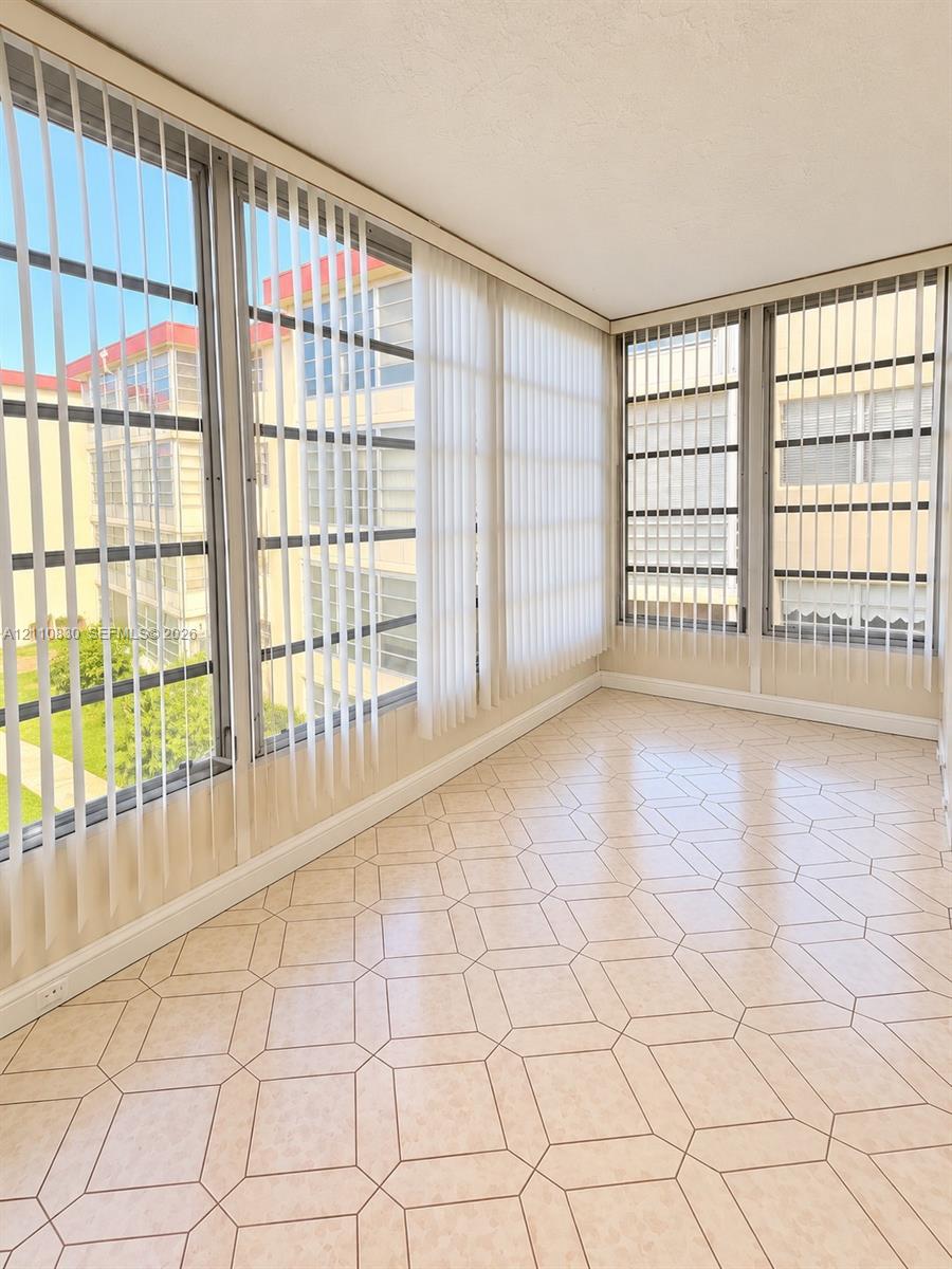 Enclosed space featuring expansive floor-to-ceiling windows, geometric-patterned tile flooring, and vertical blinds Enclosed space featuring expansive floor-to-ceiling windows, geometric-patterned tile flooring, and vertical blinds