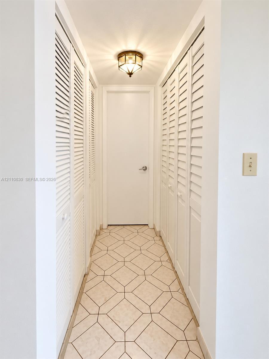 Hallway featuring geometric pattern tile flooring, multiple sets of white louvered closet doors, and a flush-mount lantern-style ceiling light fixture