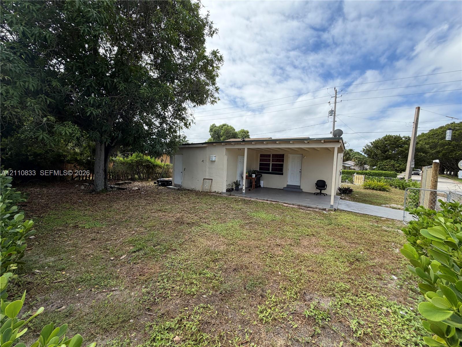 Exterior property featuring a covered patio, concrete walkway, and mature trees situated on a parcel with perimeter fencing