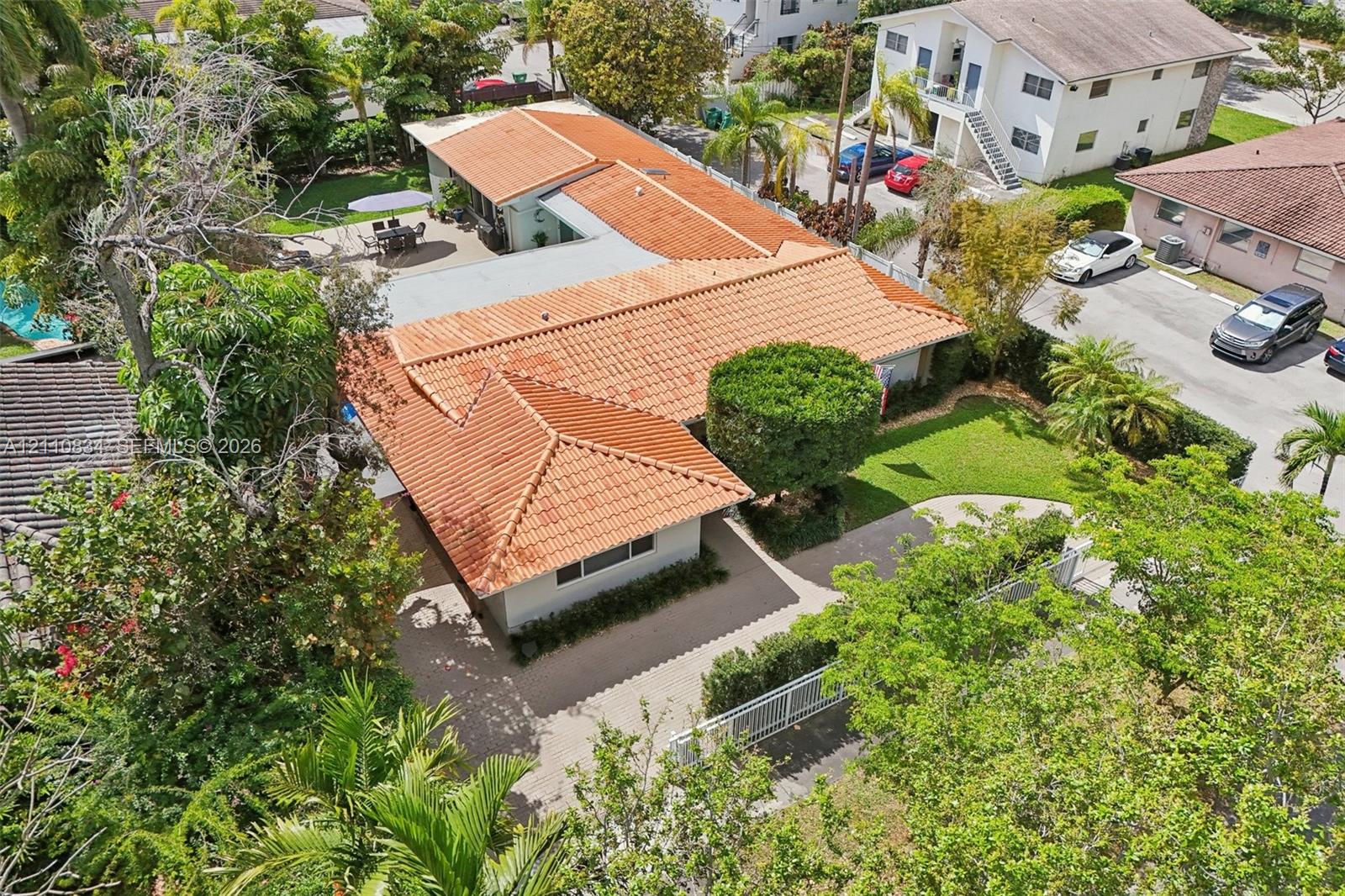 Aerial perspective of a single-story residence featuring a terracotta tile roof, paved driveway, expansive manicured lawn, and mature landscaping