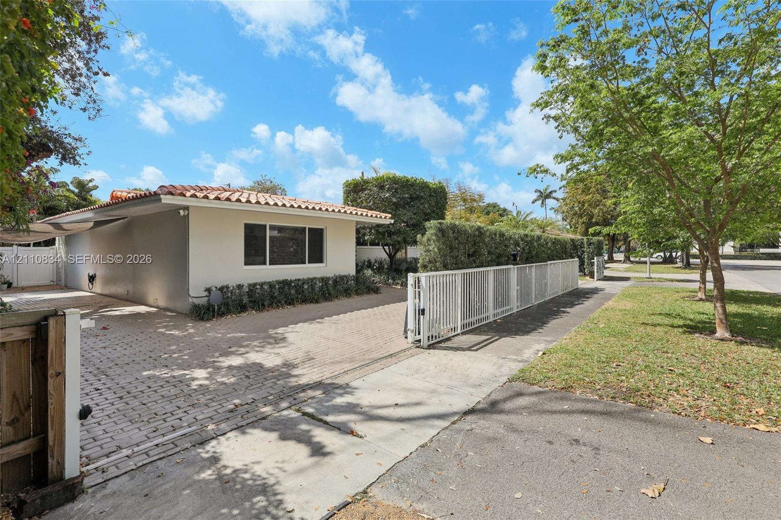 Single-story exterior featuring a clay tile roof, paved driveway, and perimeter white metal fencing