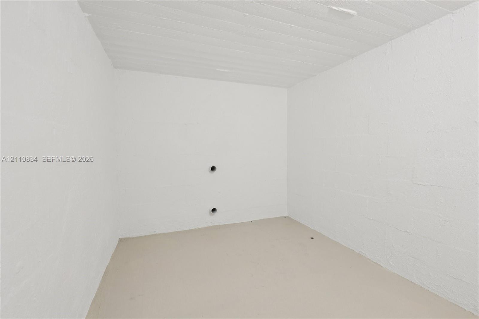 Enclosed space featuring white-painted masonry walls, a painted concrete floor, and a textured ceiling