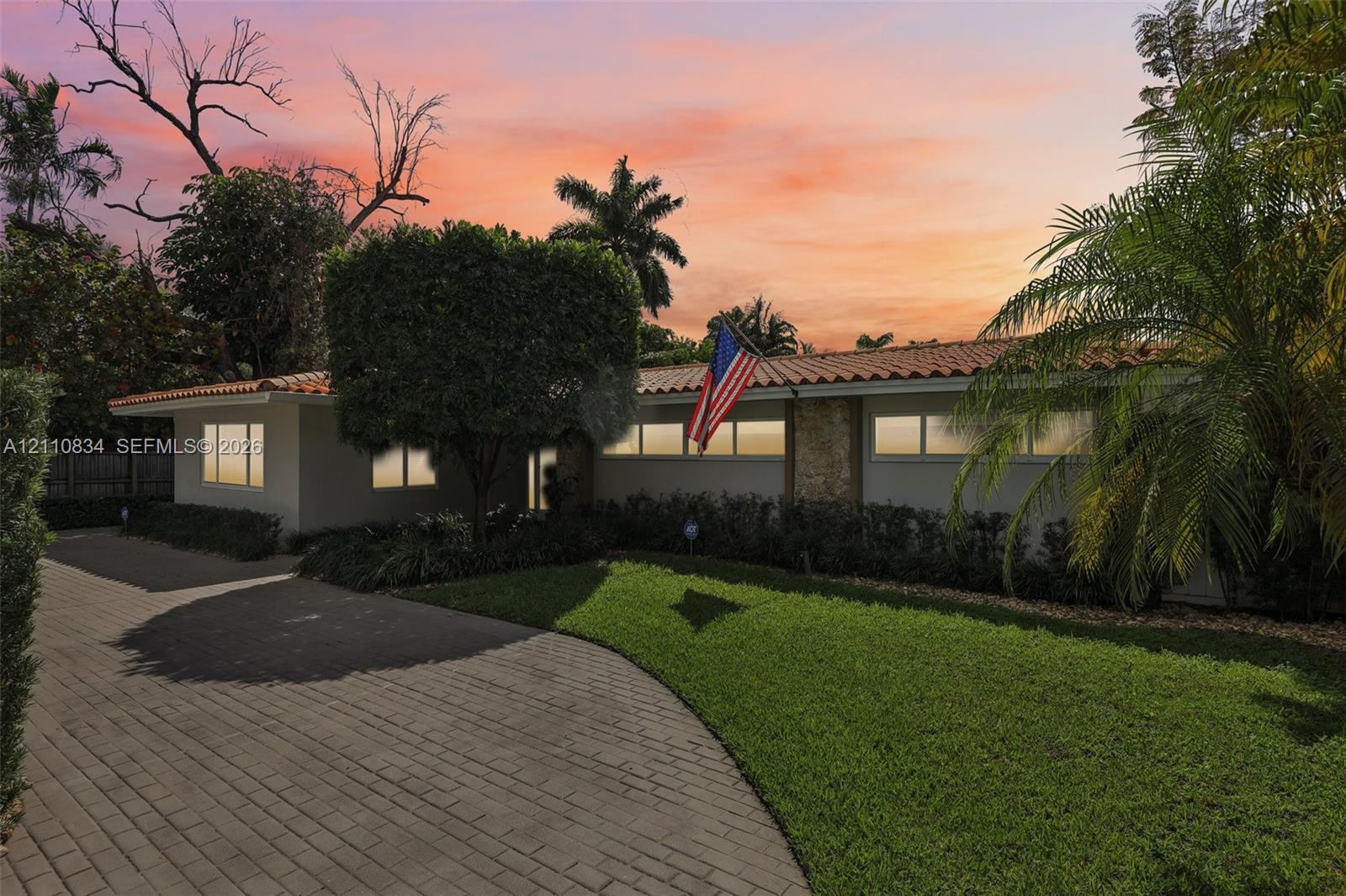 Single-story residence featuring a clay tile roof, stone masonry accents, a paved driveway, and manicured landscaping