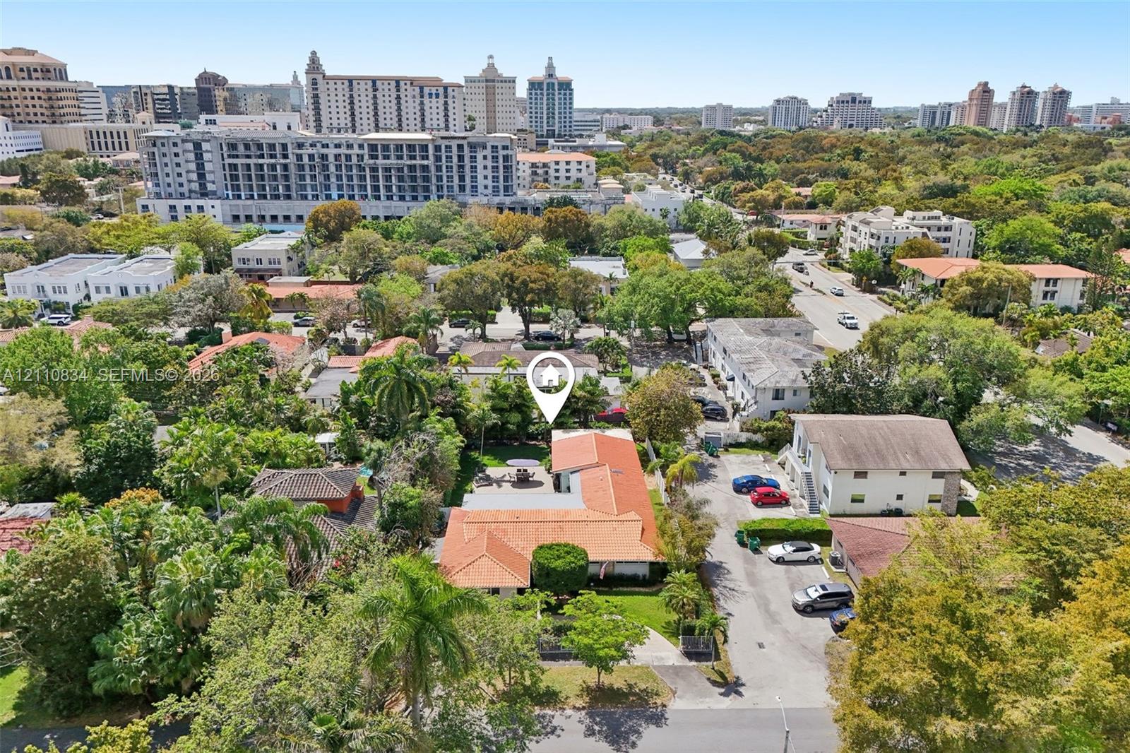 Aerial perspective featuring a terracotta-tiled roof, paved driveway, mature trees, and landscaping