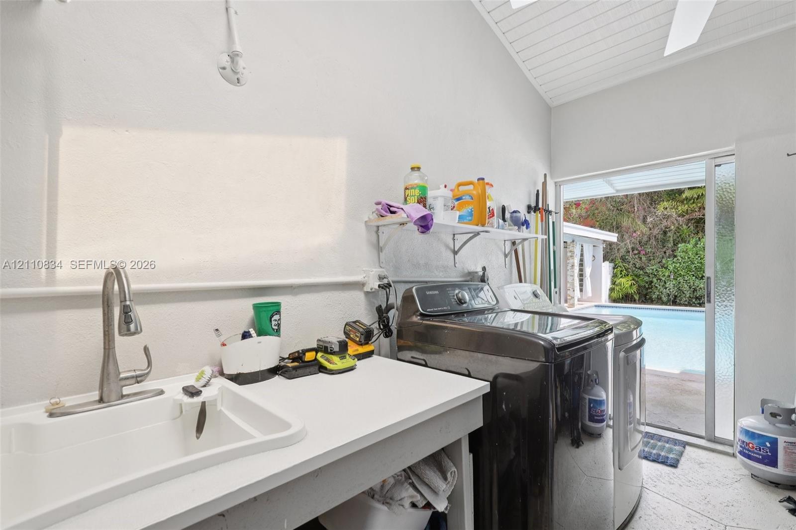 Laundry area featuring a utility sink with a high-arch pull-down faucet, vaulted ceiling with tongue-and-groove finish, tile flooring, and glass sliding door access to the exterior pool area