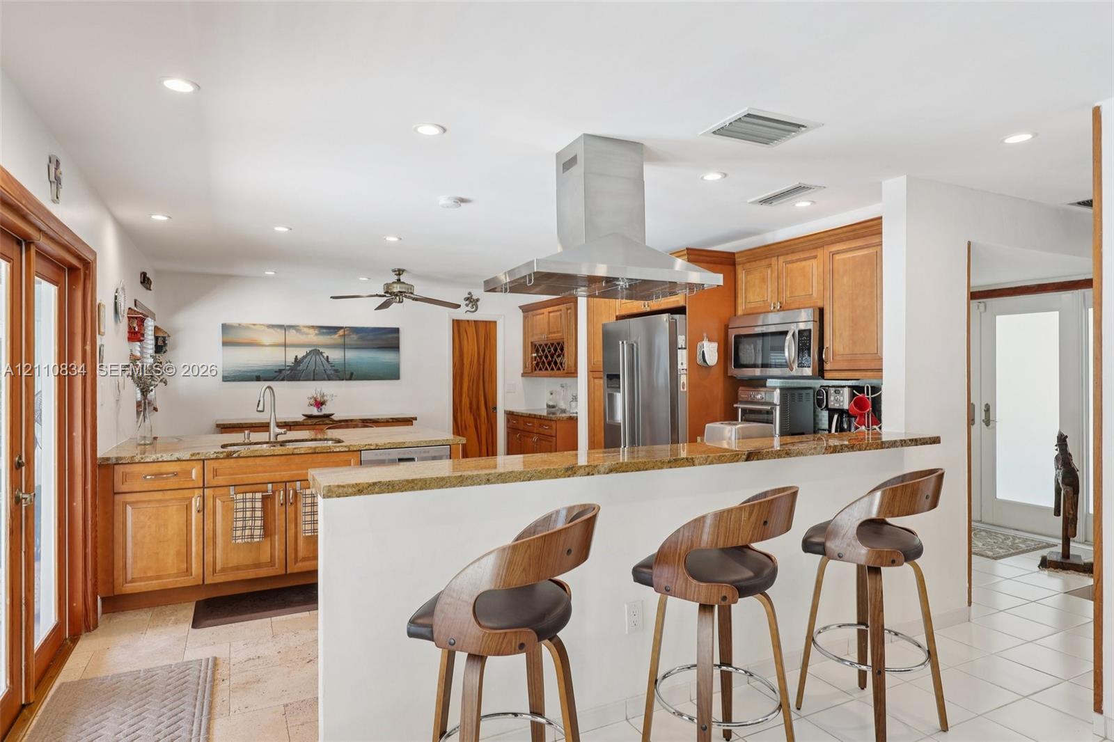 Kitchen featuring wood cabinetry, stone countertops, a raised breakfast bar, a stainless steel chimney-style range hood, and tile flooring