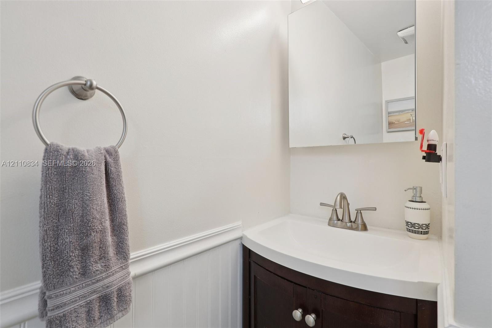 Dark wood-finish vanity with integrated sink, brushed nickel faucet, wall-mounted mirror, and white wainscoting