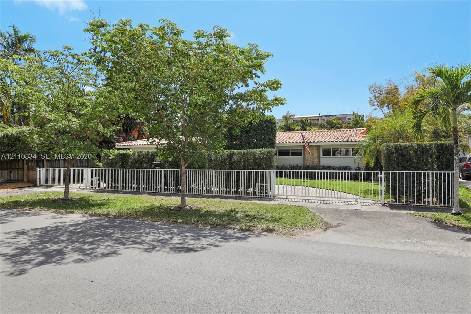 Single-story residence featuring a terracotta-tiled roof, stone-accented facade, gated paved driveway, and mature landscaping