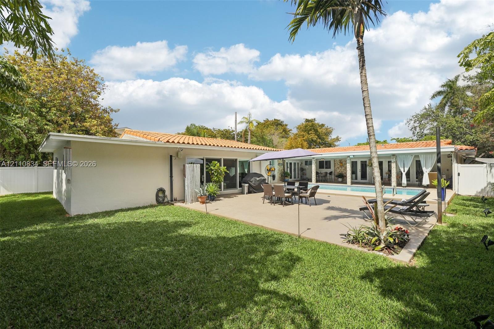 Rear exterior featuring a concrete patio, rectangular swimming pool, clay tile roof, and enclosed yard with perimeter fencing