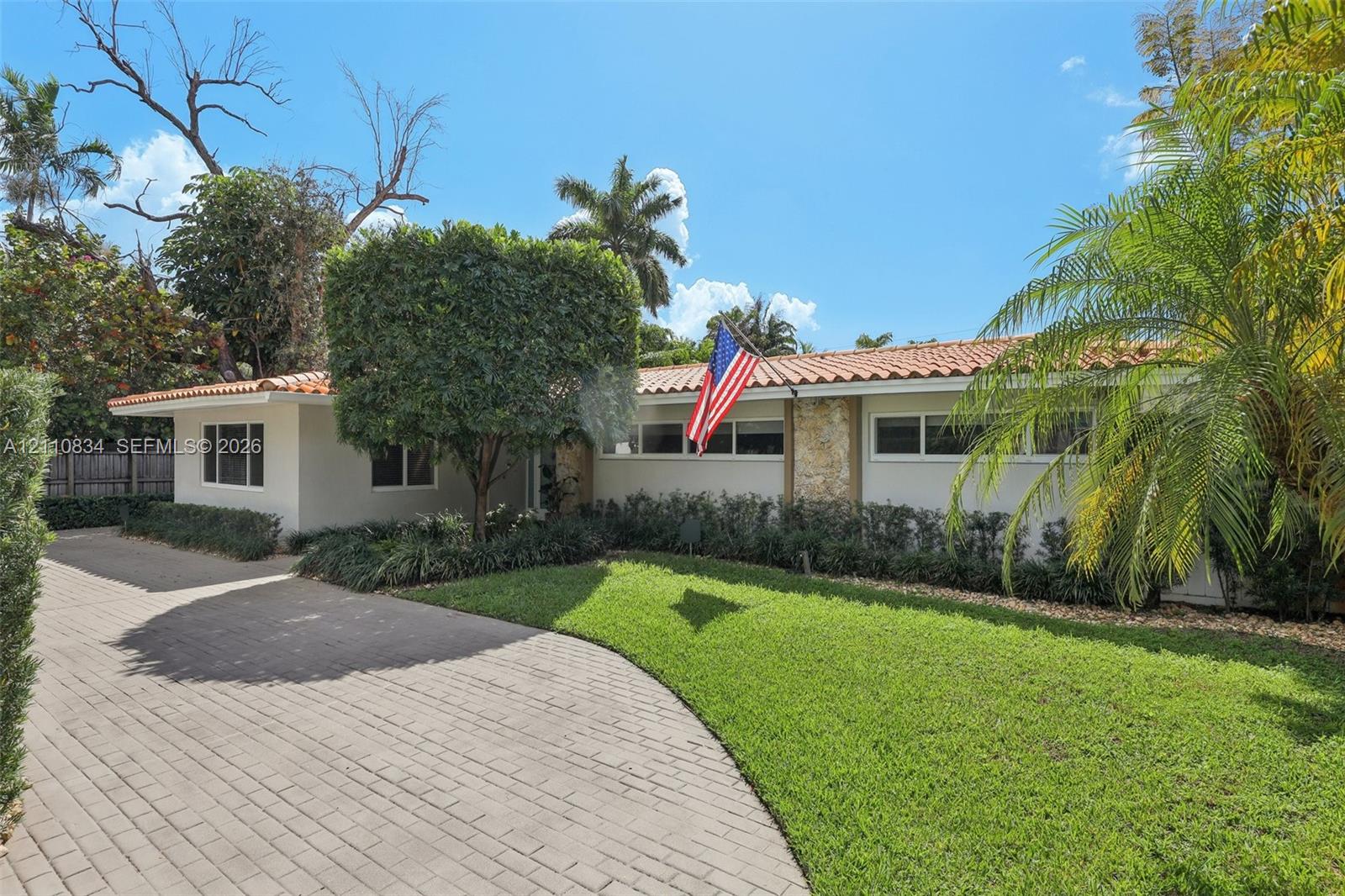 Single-story exterior featuring a clay tile roof, stone masonry facade accents, and a paved brick driveway