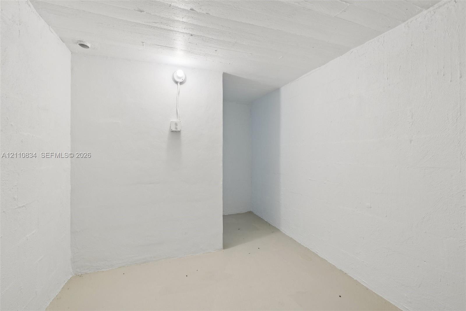 Enclosed space featuring painted masonry walls, a concrete floor, exposed ceiling joists, and an electrical wall outlet