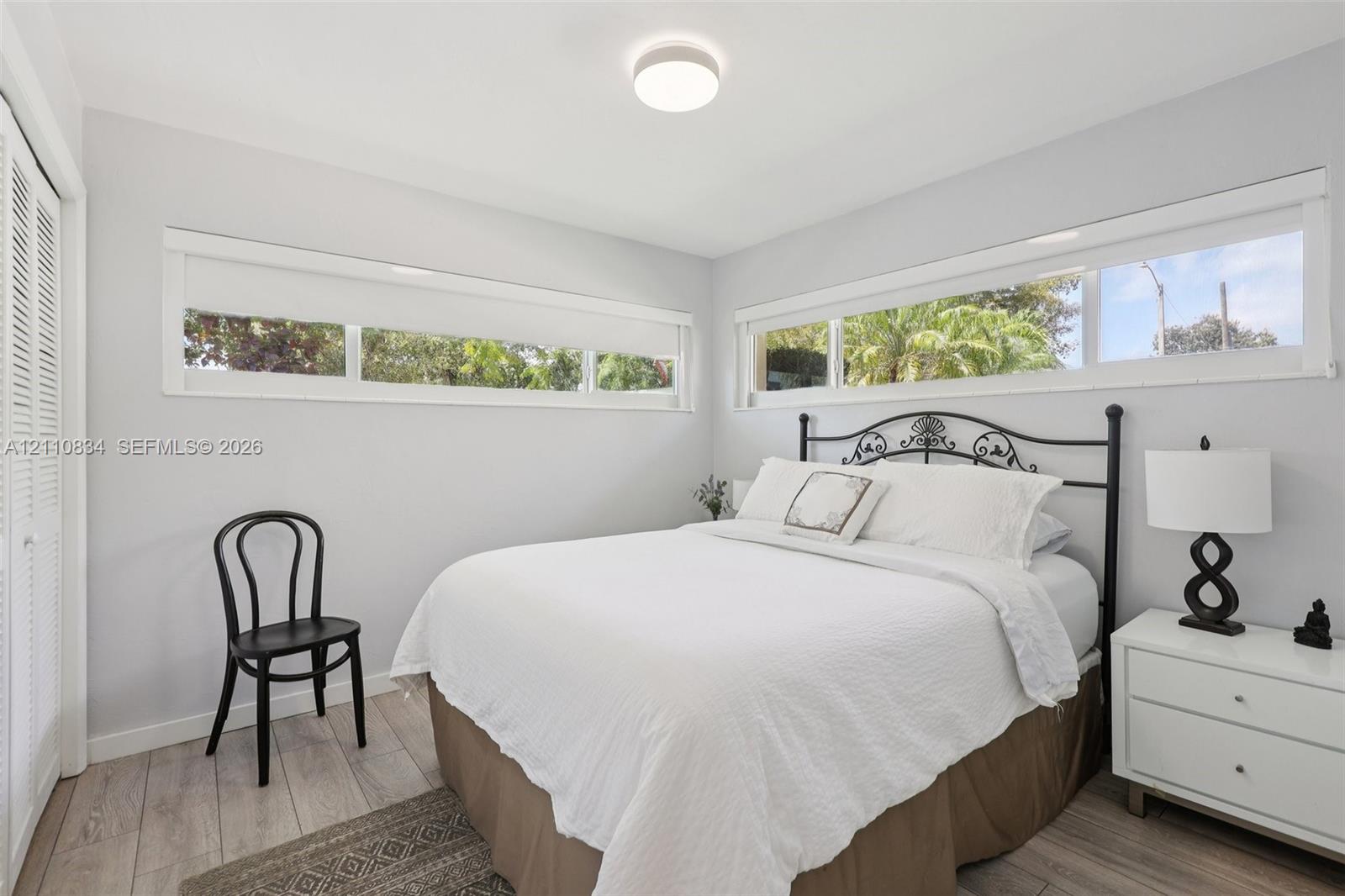 Neutral-toned interior featuring wood-finish flooring, horizontal sliding windows, and a built-in closet with bi-fold louvered doors