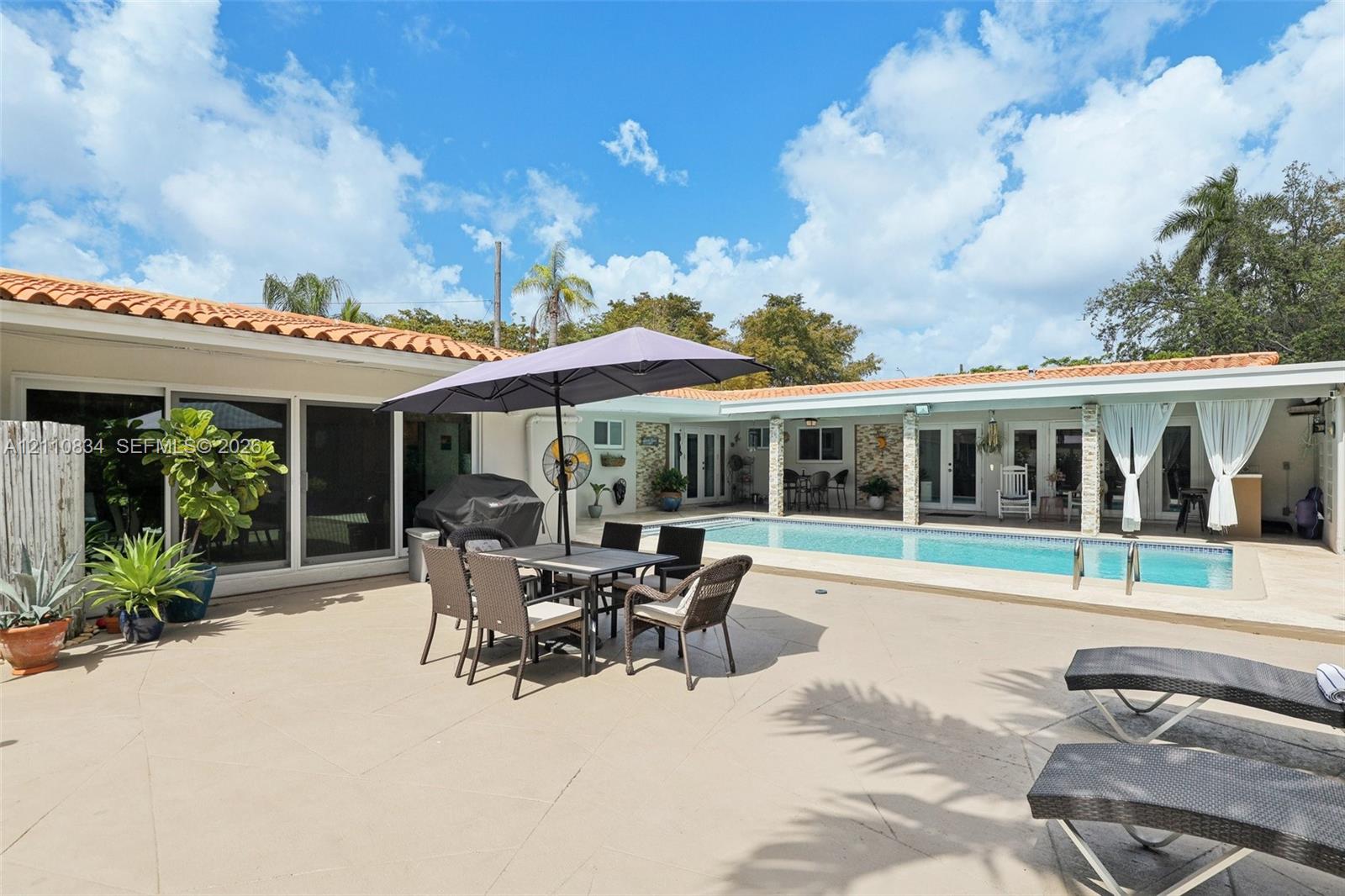 Extensive paved patio featuring an in-ground swimming pool, clay tile roof, and covered outdoor area with stone column supports