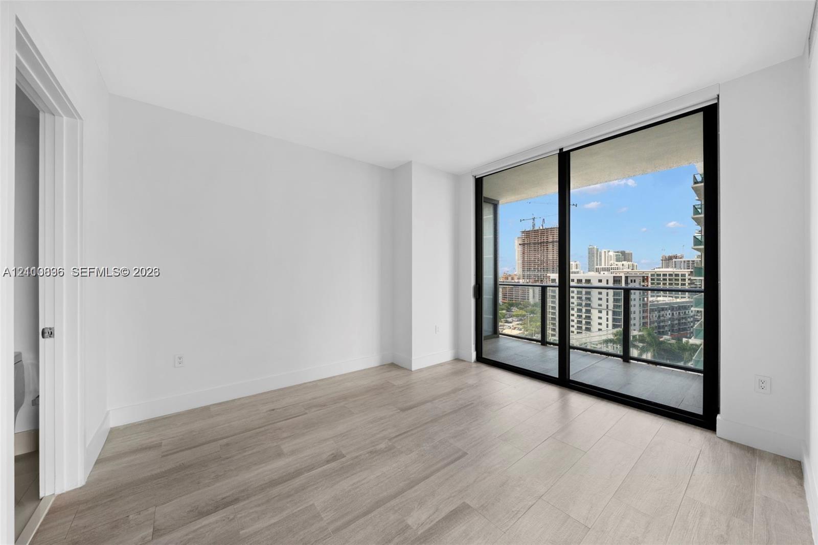 Floor-to-ceiling sliding glass doors, private balcony, wood-finish flooring, and expansive urban scenery