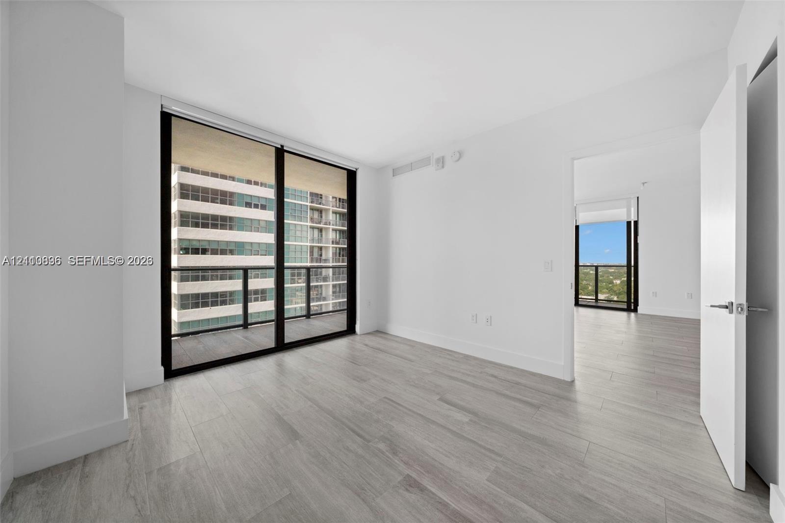 Floor-to-ceiling sliding glass doors, private balcony, wood-finish flooring, and minimalist white interior finishes