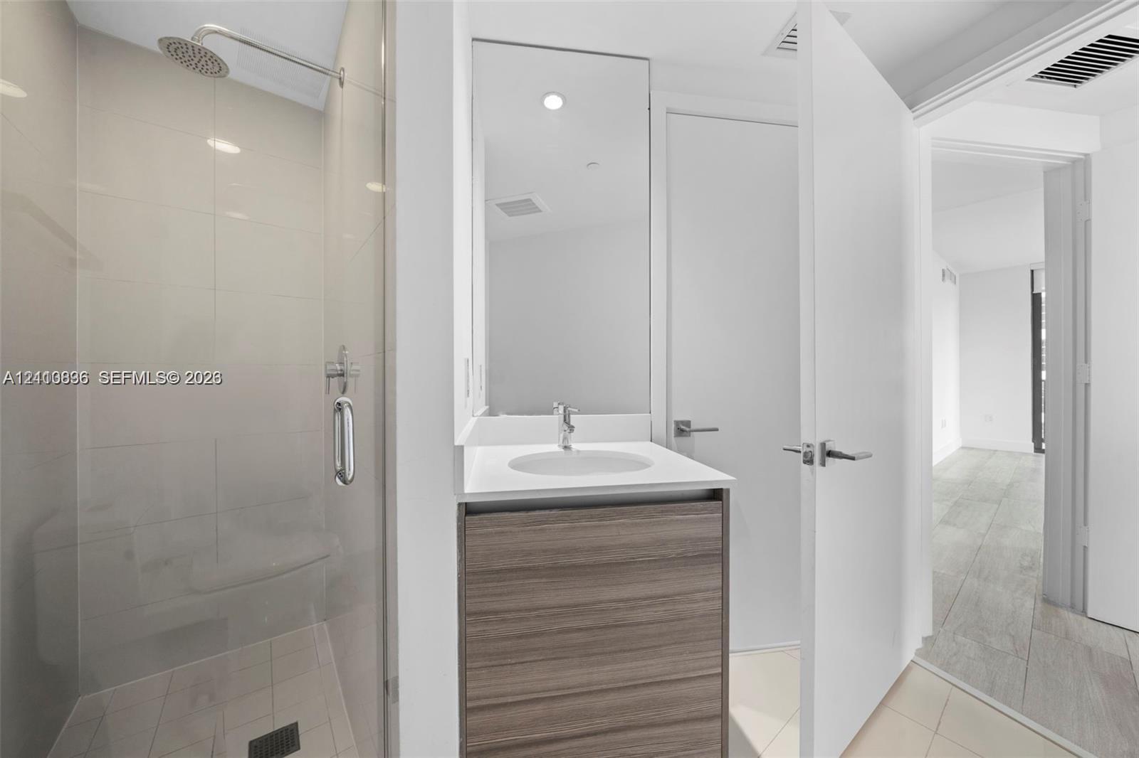Glass-enclosed shower with rainfall showerhead, wood-finish vanity with countertop basin, and large-format tile flooring