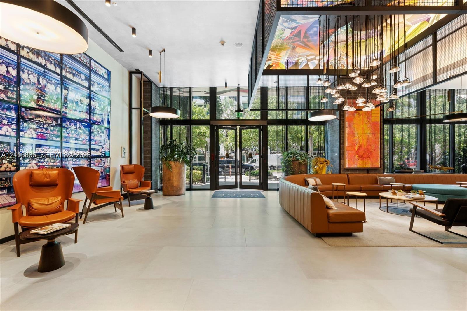 Floor-to-ceiling glass entry doors, large-format tile flooring, industrial-style multi-pendant lighting, recessed ceiling fixtures, and expansive wall-mounted mural installation
