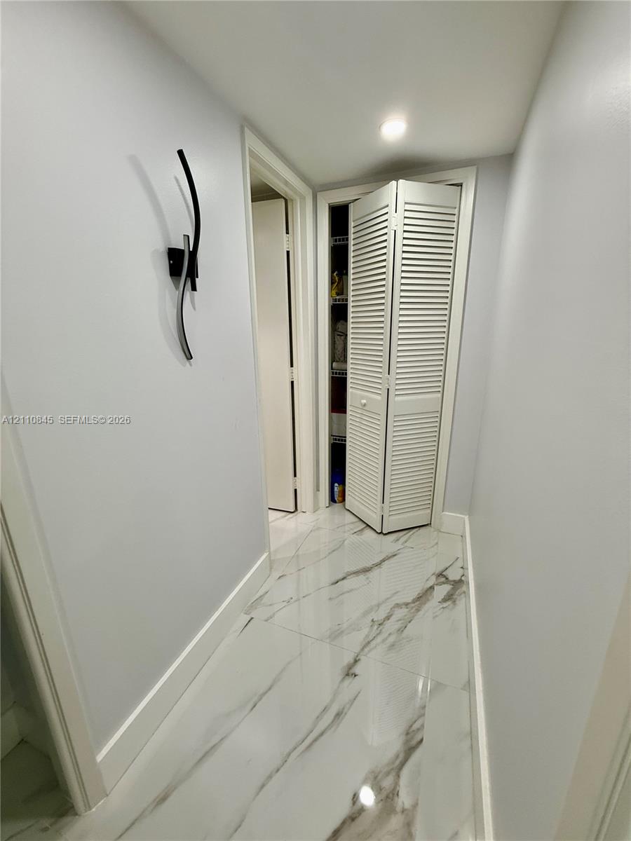 Large-format tile flooring with a neutral-toned veined pattern, louvered bi-fold closet doors, and a contemporary wall-mounted light fixture