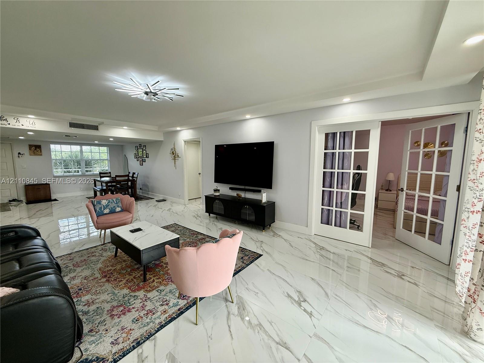 Open-concept interior featuring polished stone-finish flooring, recessed lighting, a modern starburst chandelier, and French doors with glass panes