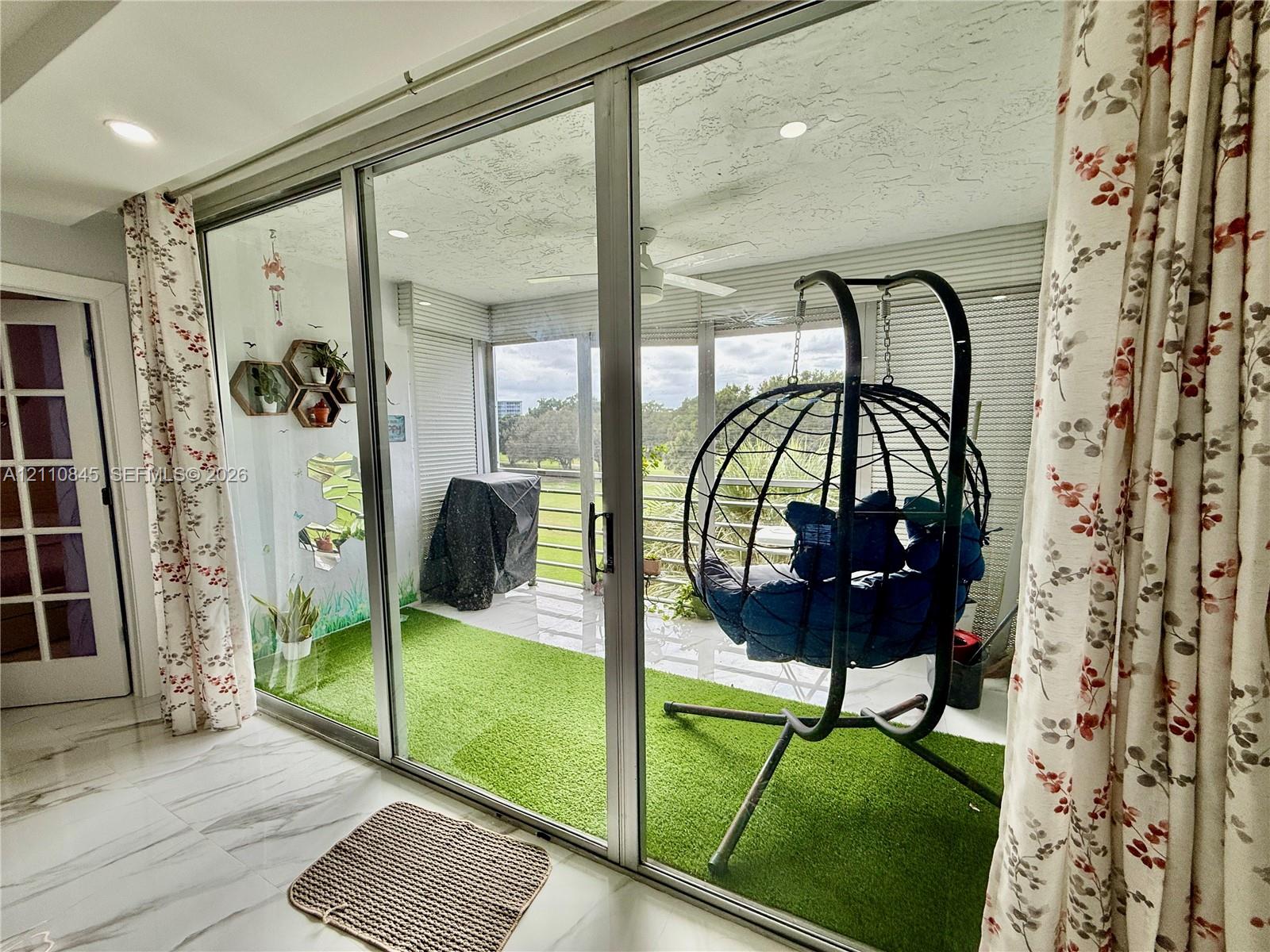 Enclosed balcony featuring floor-to-ceiling glass sliding doors, synthetic turf flooring, ceiling fan, and metal railings