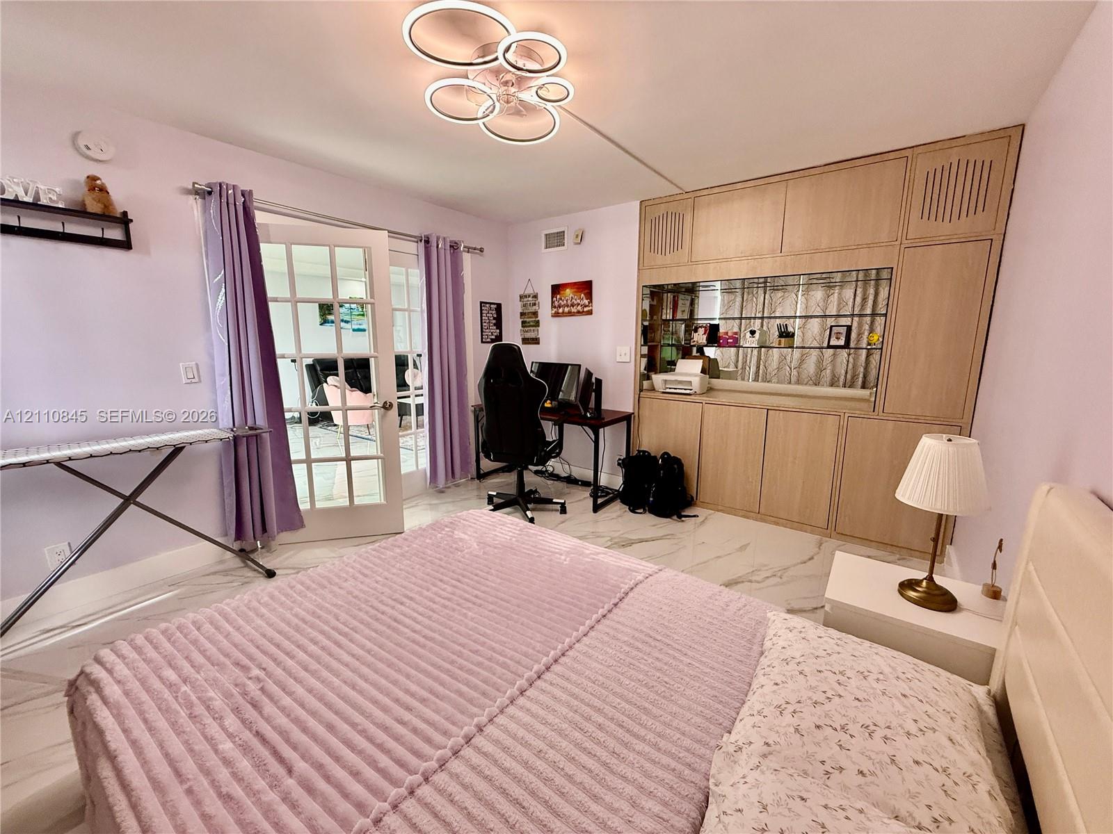 Large-format tile flooring, integrated floor-to-ceiling wooden cabinetry with a built-in mirrored display section, multi-tiered circular LED light fixture, and double French doors with glass panes