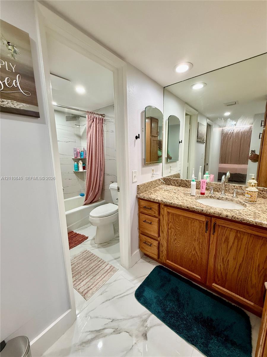 Vanity with stone countertop, wood-finish cabinetry, full-width mirror, recessed lighting, and tile flooring