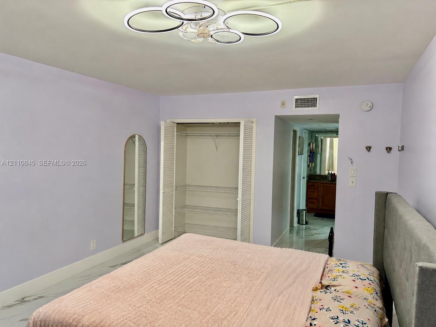 Multi-ring LED flush-mount fixture, closet with louvered bi-fold doors and integrated shelving, and large-format tile flooring