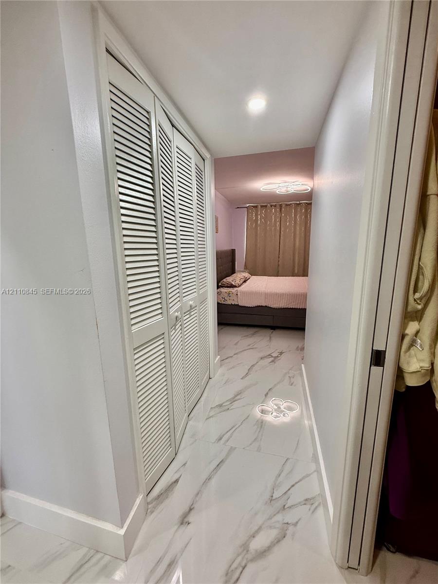 Hallway featuring large-format tile flooring with a neutral-toned pattern, recessed ceiling lighting, and floor-to-ceiling louvered closet doors