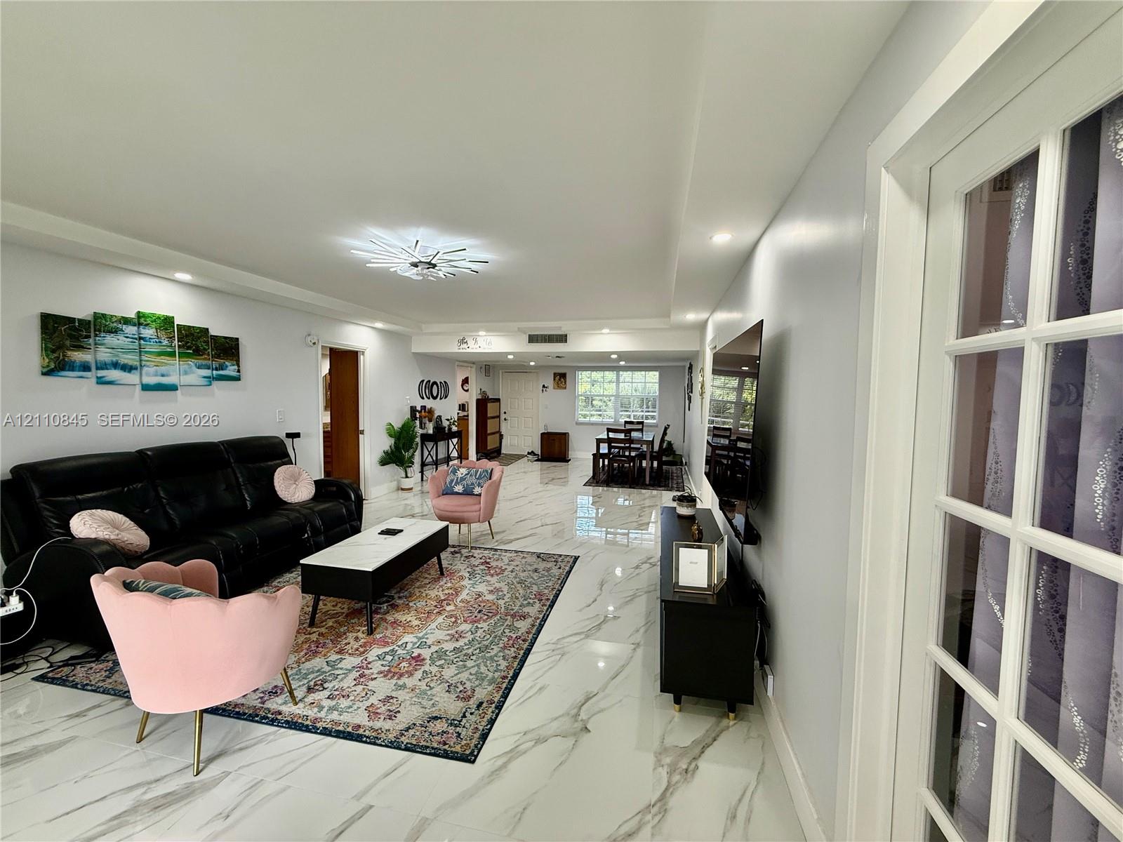 Open-concept living space featuring large-format tile flooring with vein detailing, recessed ceiling lighting, a multi-arm modern light fixture, and white French doors