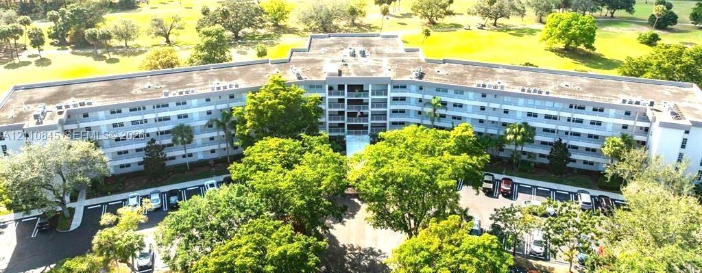 Multi-story residential building featuring private balconies, expansive grounds with mature trees, and surface parking