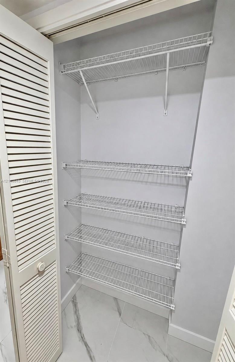 Storage area featuring louvered bi-fold doors, four-tier ventilated wire shelving, and stone-finish flooring