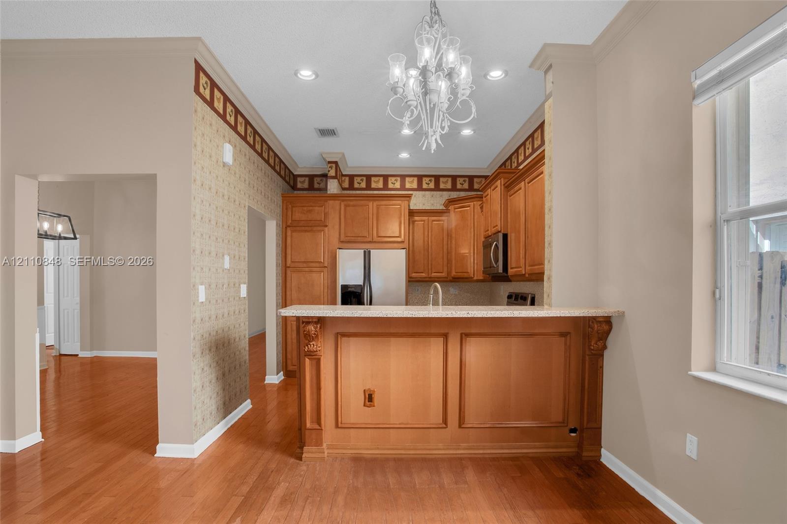 Kitchen featuring wood-finish cabinetry, a raised breakfast bar with stone-surfaced countertop, recessed lighting, and a decorative chandelier