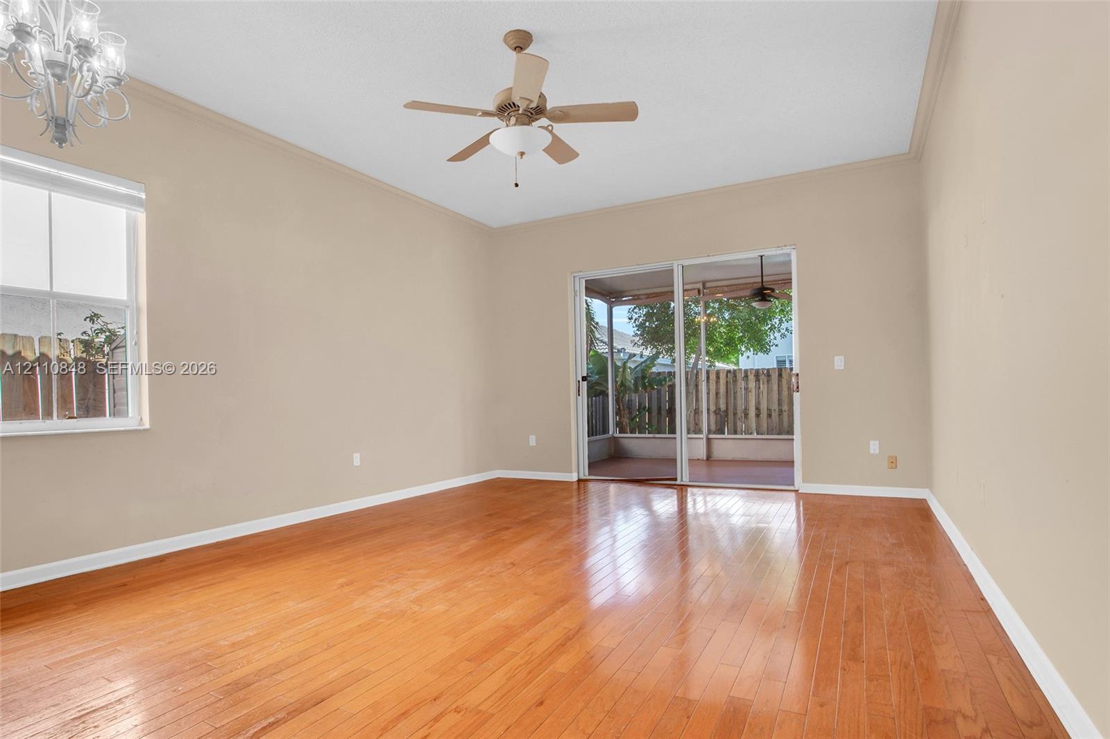 Wood-finish flooring, sliding glass door, ceiling fan, crown molding, and decorative light fixture