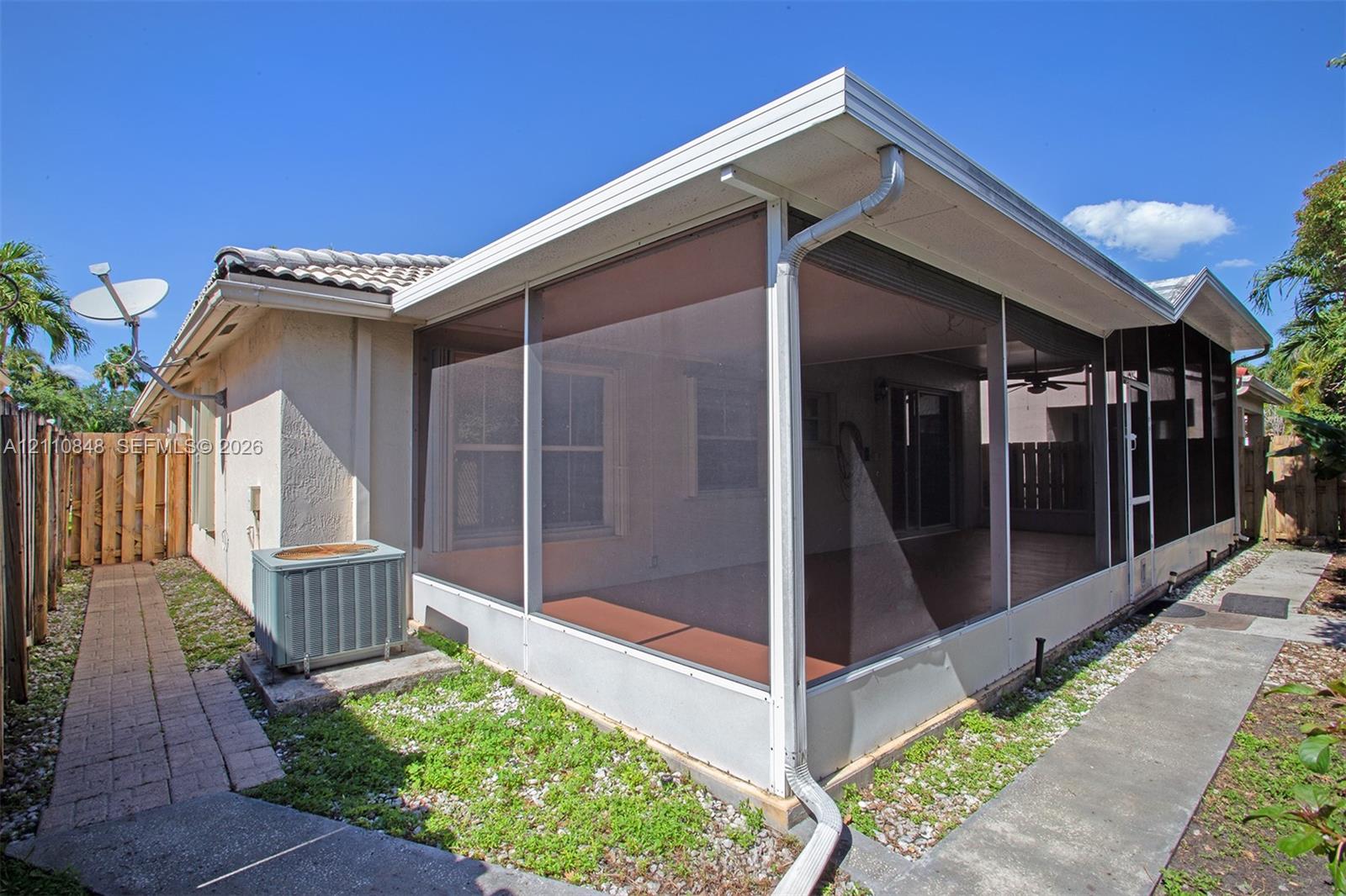 Screened-in rear porch featuring a tile-finish floor, white aluminum framing, concrete walkways, and a wood privacy fence