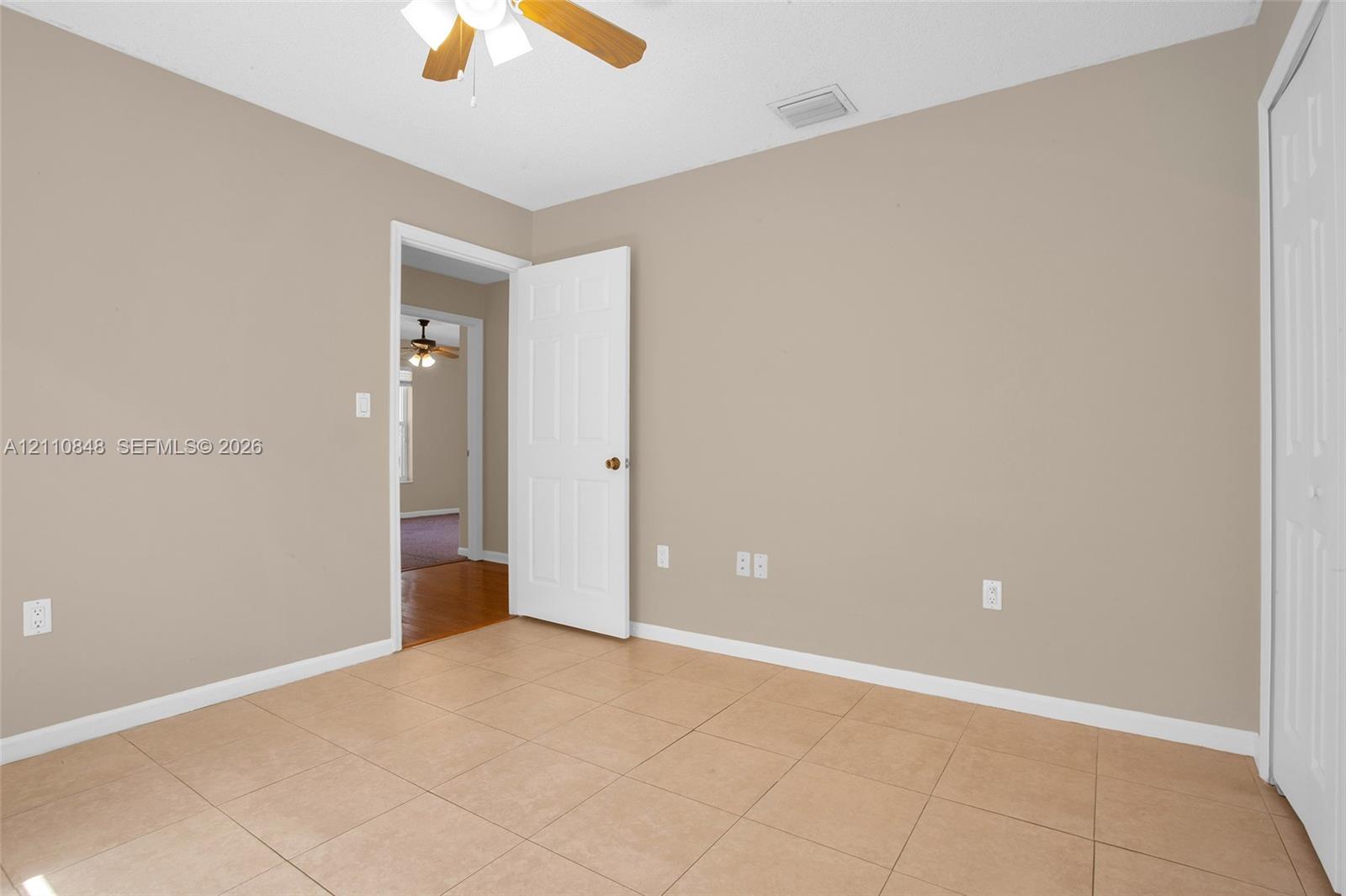 Room featuring tile flooring, neutral wall tones, a ceiling fan with light fixture, and a built-in closet with double doors
