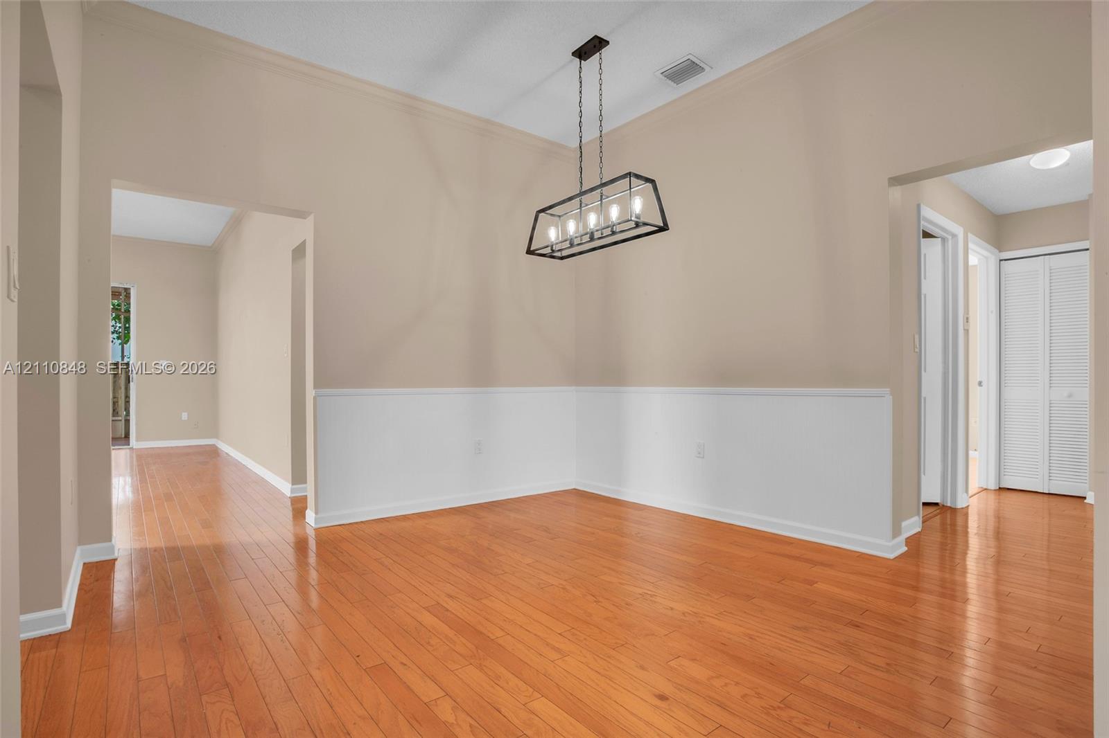 Wood-finish flooring, half-wall wainscoting, and a linear cage-style chandelier