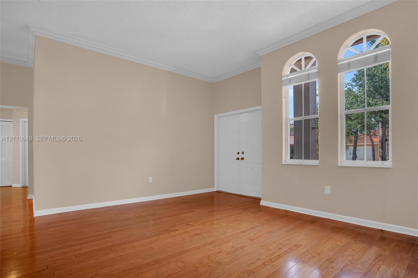 High-ceiling interior featuring wood-finish flooring, dual arched windows, and double door entry