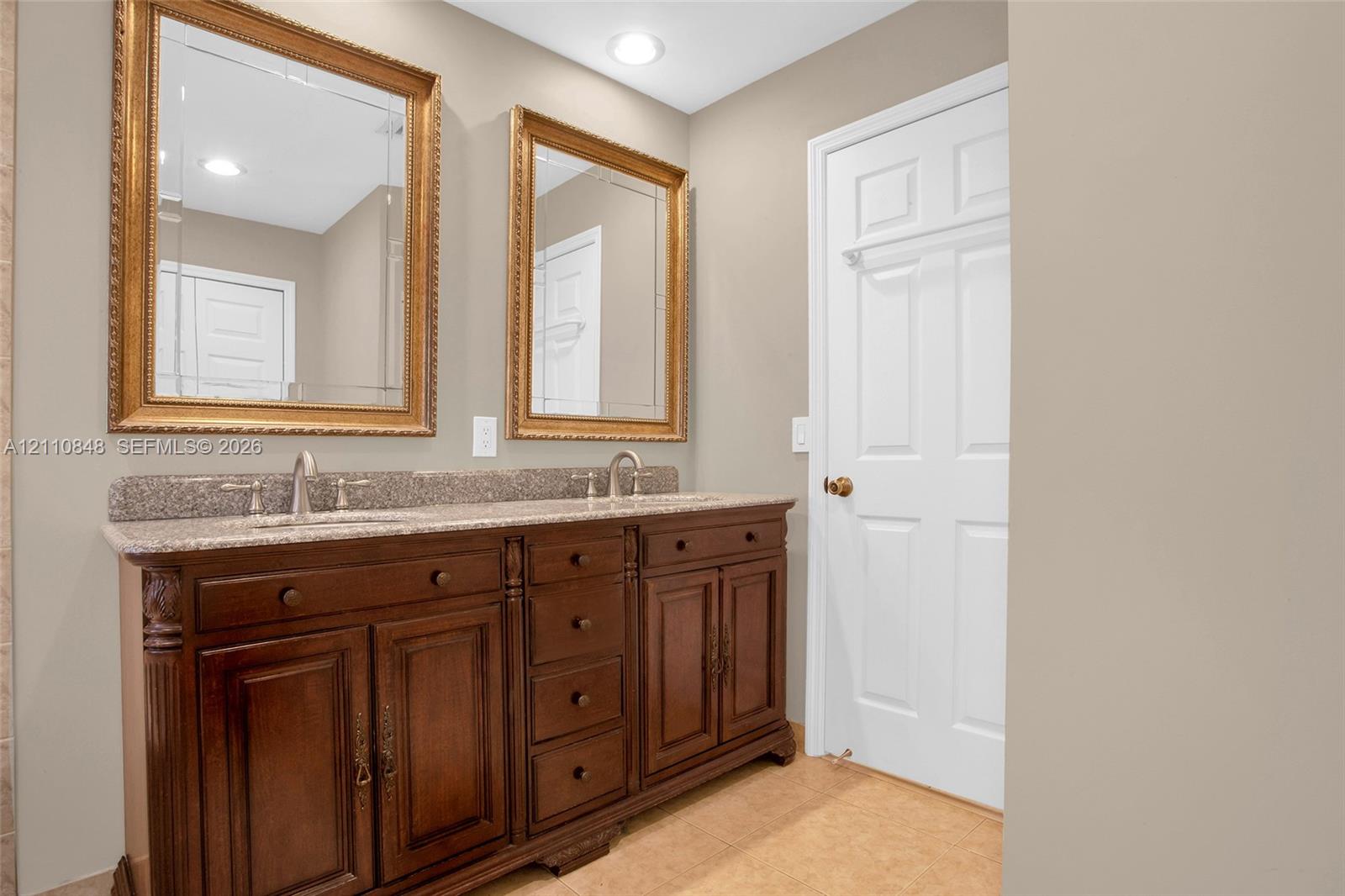 Double-sink vanity with wood cabinetry, stone-finish countertop, dual wall-mounted framed mirrors, and six-panel interior door