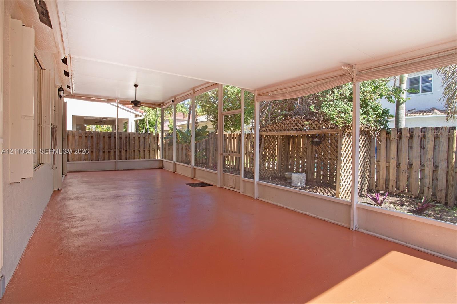 Screened-in patio featuring a solid-surface floor, ceiling-mounted fan, and wooden perimeter fencing