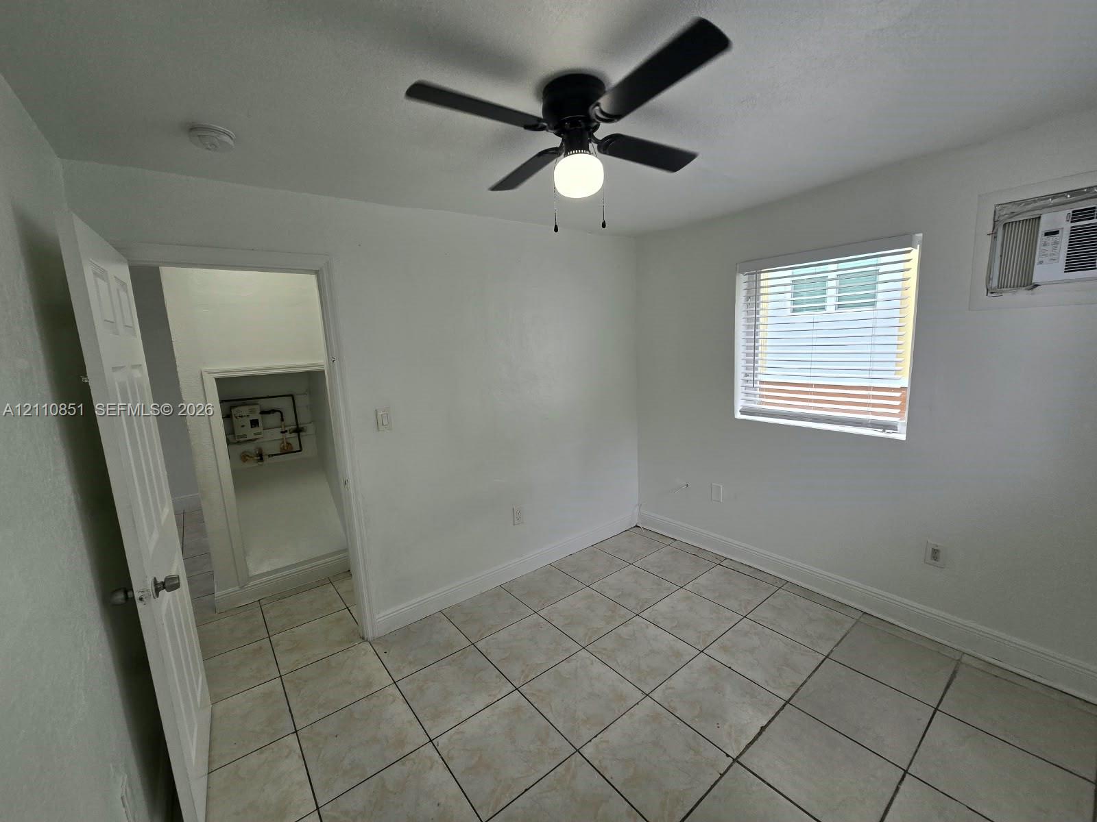 Neutral-toned tile flooring, white wall finish, ceiling fan with integrated lighting, and a multi-pane window with blinds