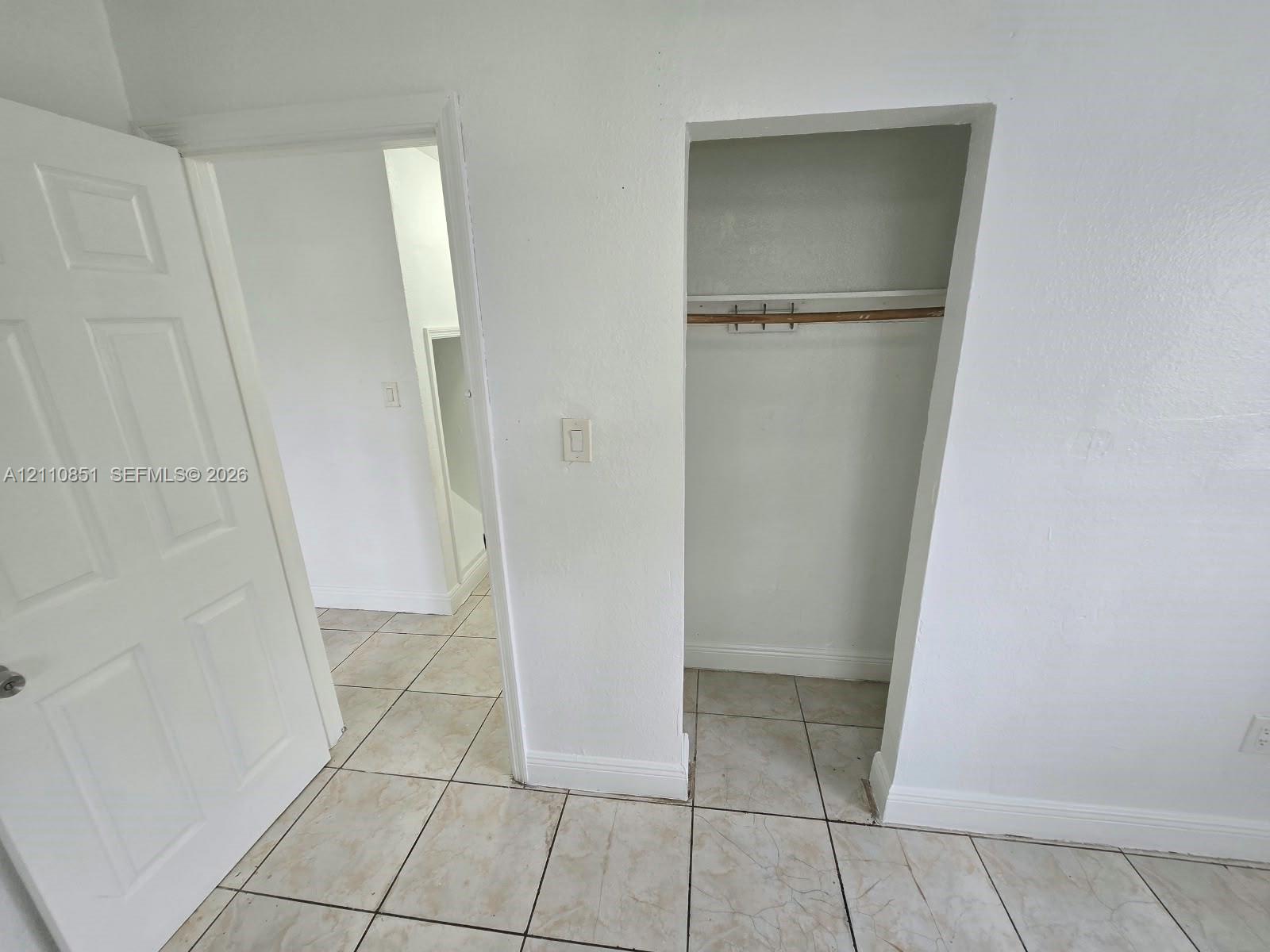 Interior space featuring ceramic tile flooring, a six-panel door, and a built-in closet with a shelf and hanging rod