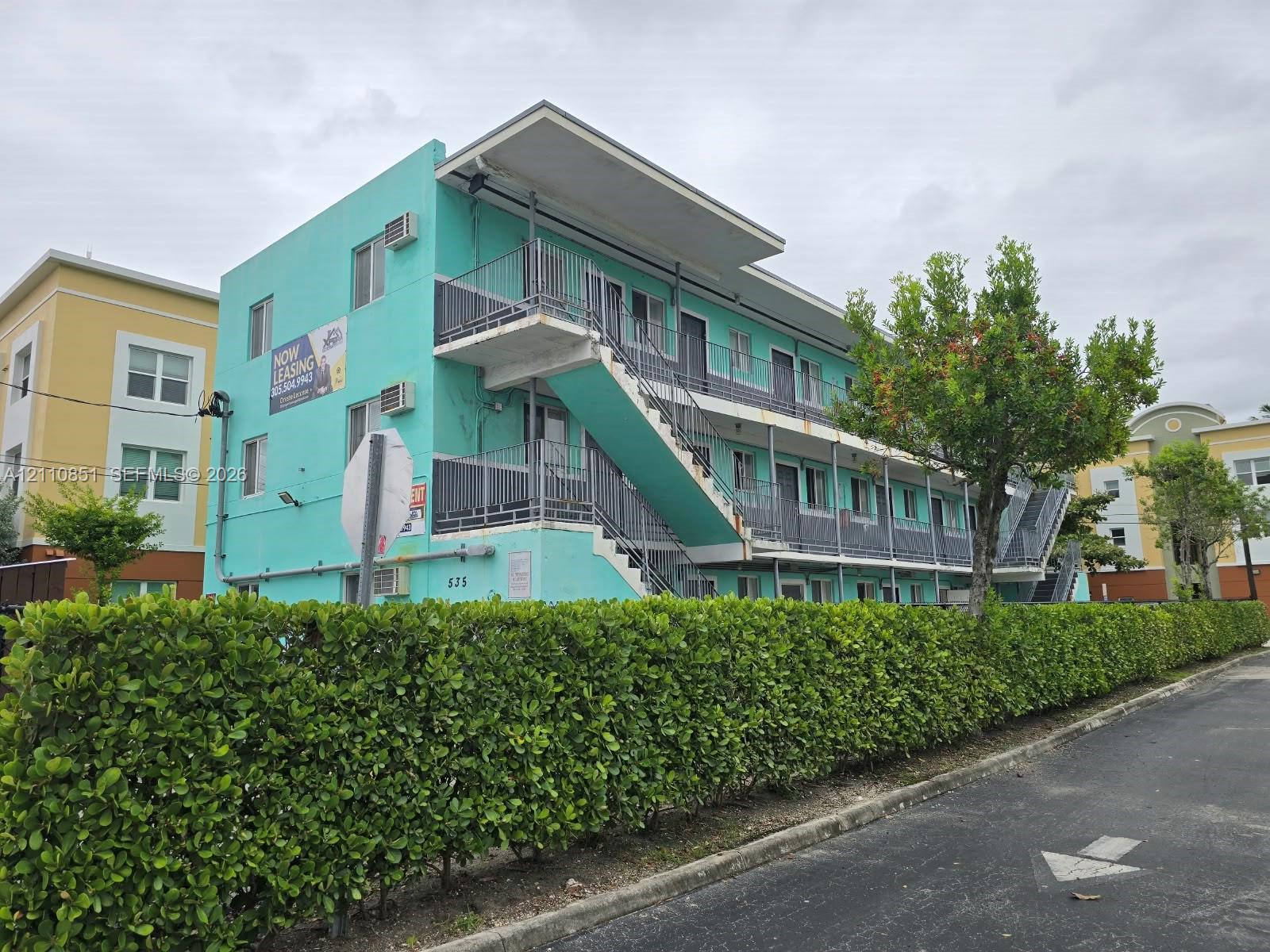 Three-story exterior featuring a flat roofline, metal exterior staircases, railed balconies, and a manicured hedge perimeter